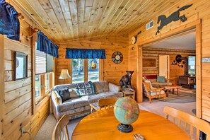 L’intérieur d’un chalet confortable, avec des murs en rondins de bois, un canapé, une table à manger surmontée d’un globe terrestre, une statue d’ours et une cheminée.