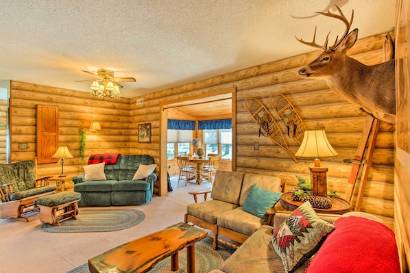 L’intérieur d’une cabane en rondins, avec une tête de cerf accrochée au mur, des meubles en bois et une cheminée chaleureuse.