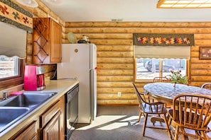 Une cuisine aménagée dans un chalet en rondins, comprenant un réfrigérateur, une machine à café, un évier et une table à manger avec des chaises.