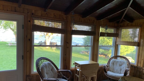 A wooden cabin interior with large windows, wicker chairs, a small table, and a lamp. - Waterfront Cottage on the bay in Green Bay (Little Suamico)