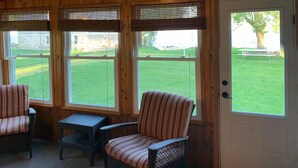 A room with a wooden ceiling, a door, and three windows. There are two wicker chairs and a small table. - Waterfront Cottage on the bay in Green Bay (Little Suamico)