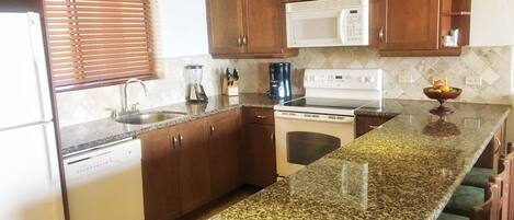 A kitchen with granite countertops, wooden cabinets, a white stove, a microwave, and a coffee maker.