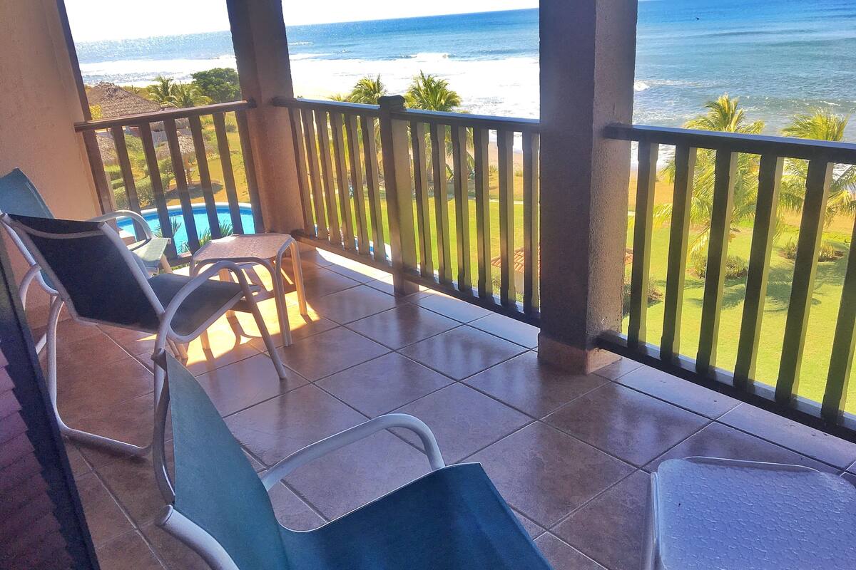 Un balcon avec deux fauteuils et une petite table, donnant sur une plage et l’océan.