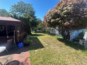 A backyard with a wooden deck, a lawn, and a tree with white flowers. - Home rental close to DT and Uvic (Victoria)