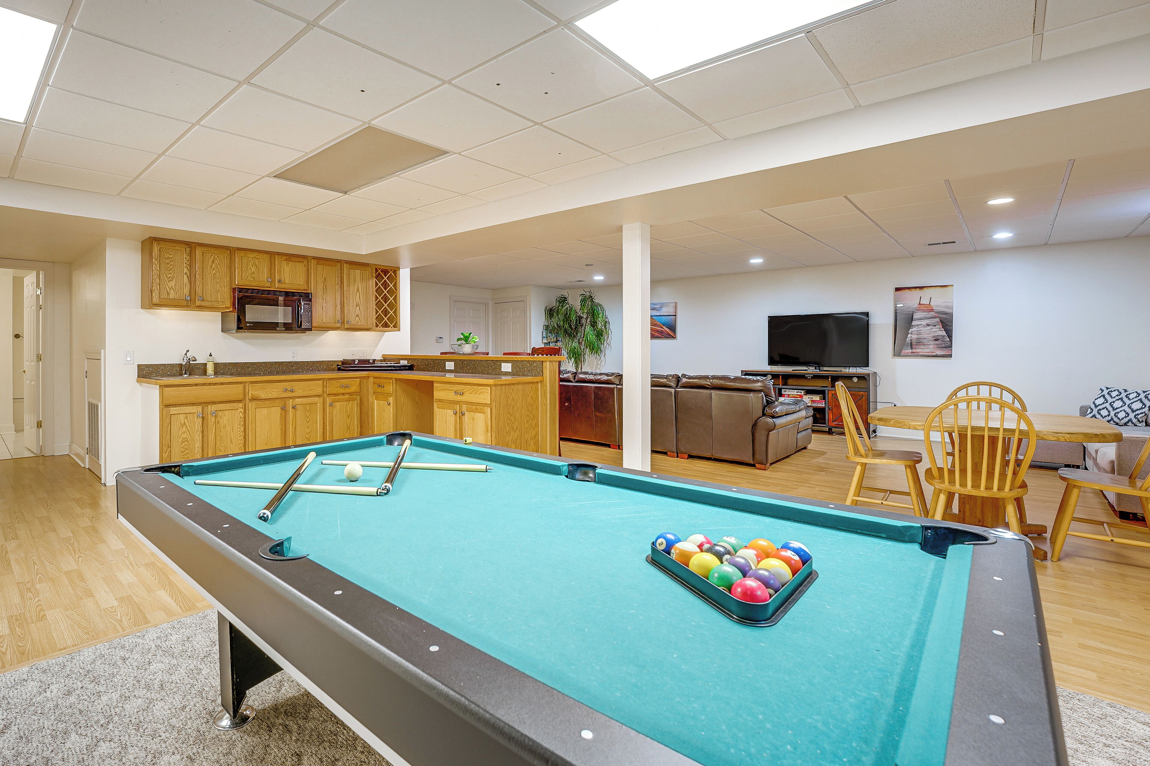 Une table de billard avec des billes, un four à micro-ondes, des meubles en bois, un téléviseur et un coin repas avec des chaises.