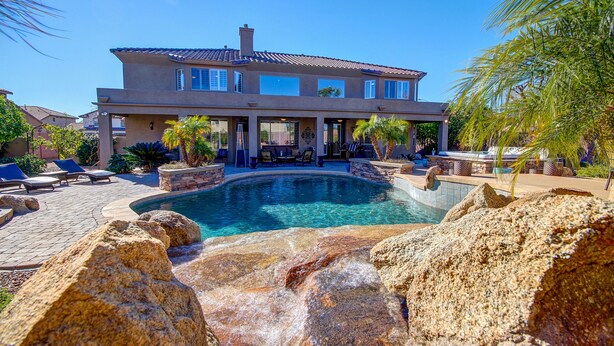 A large house with a swimming pool surrounded by rocks and palm trees.