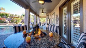 A covered outdoor seating area with a fire feature, pool, and patio furniture.