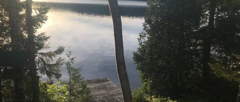 A view of a lake surrounded by trees, with a wooden deck in the foreground.