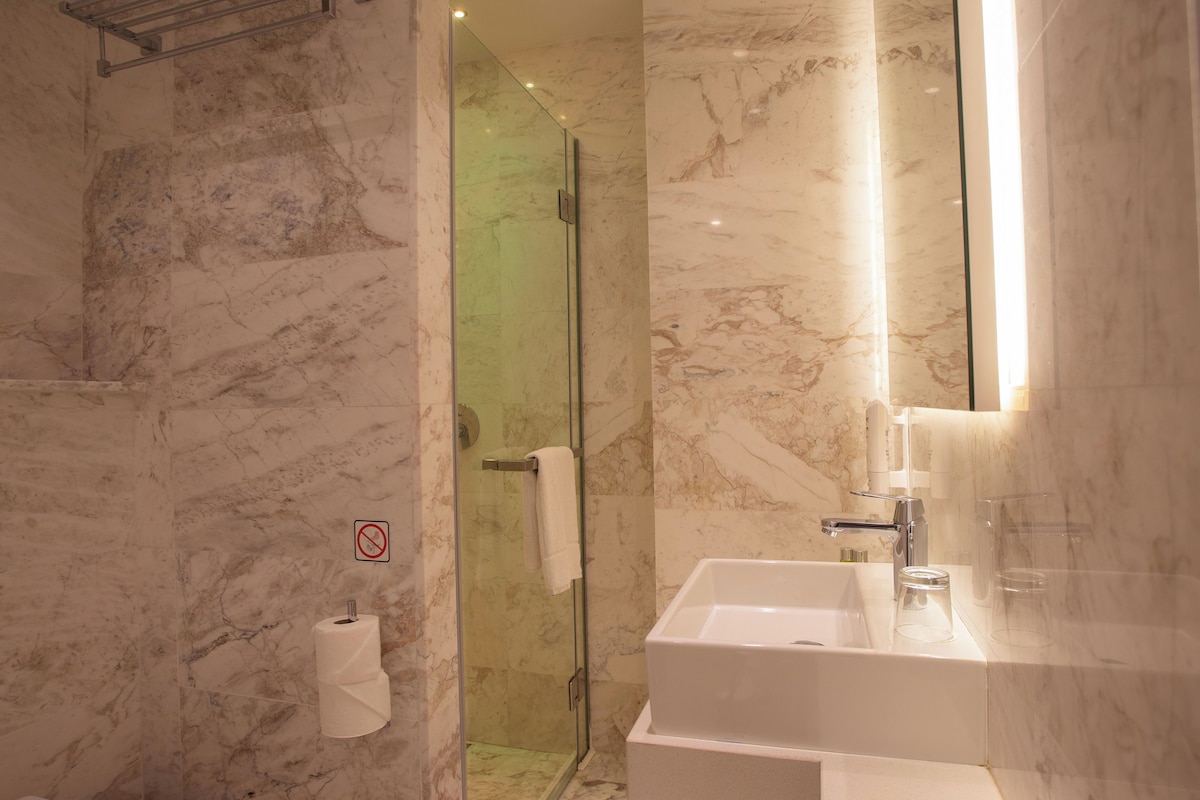 A modern bathroom with a glass shower enclosure, a white sink, and marble walls.