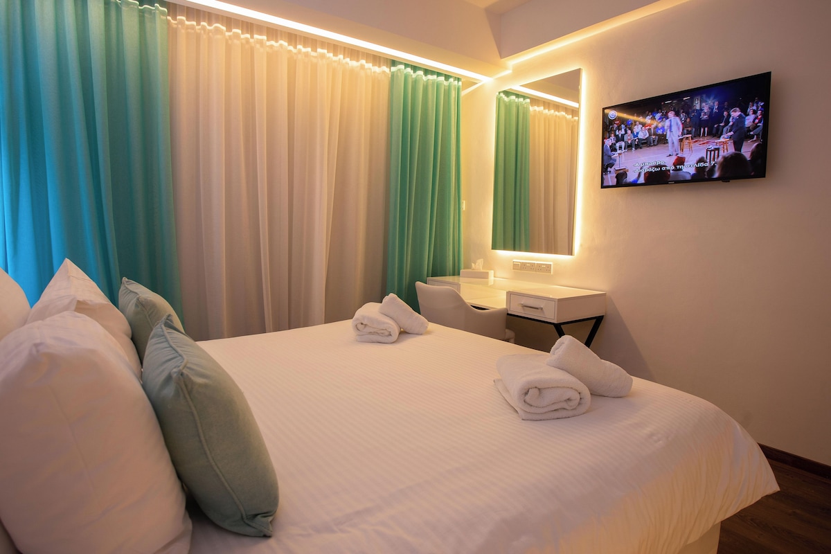 A hotel room with a bed, pillows, a TV, a desk, and a mirror.