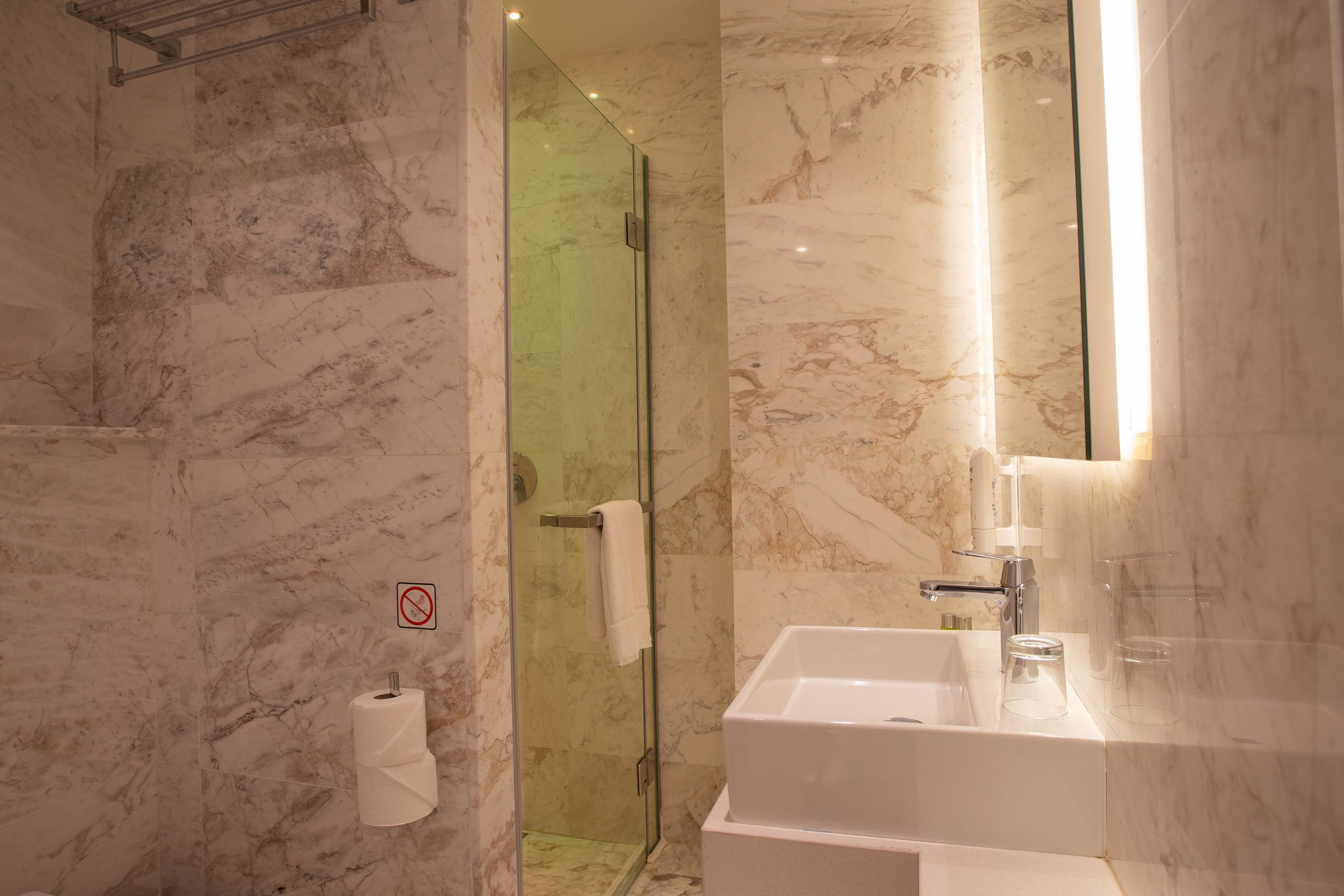 A modern bathroom with a glass shower enclosure, a white sink, and marble walls.