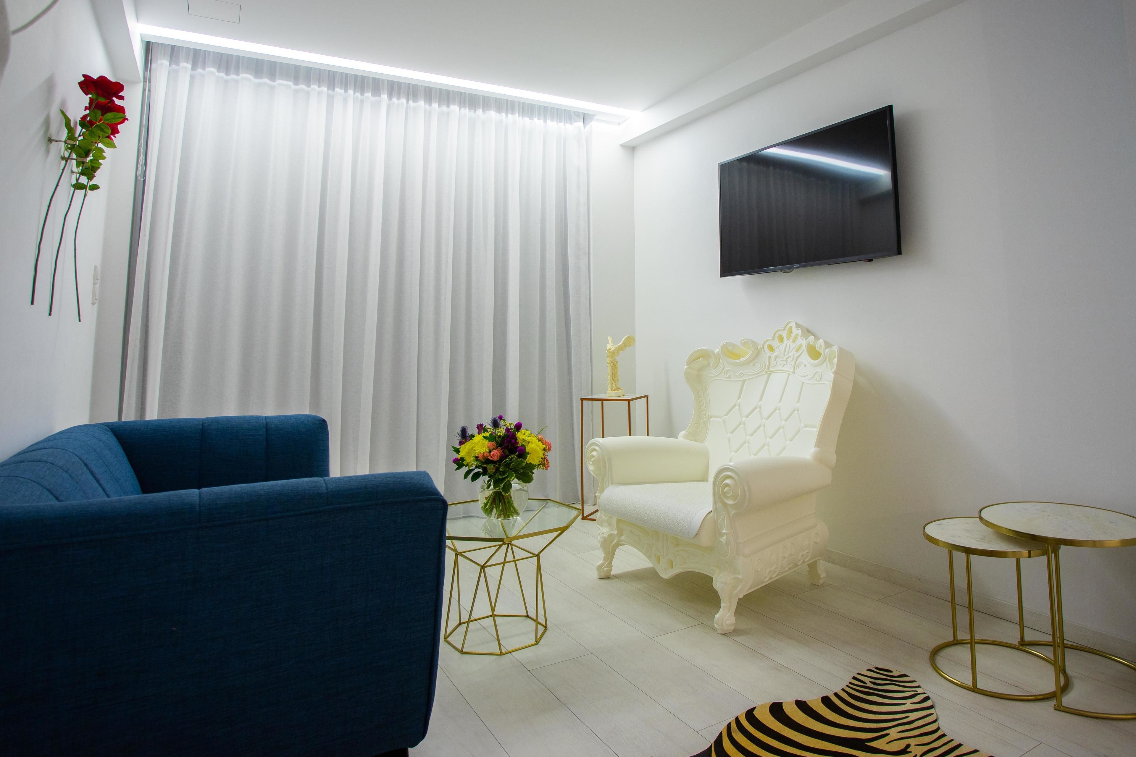 Un salon moderne avec un canapé bleu, un fauteuil blanc, une table basse en verre, un tapis à motifs zébrés et un téléviseur à écran plat fixé au mur.