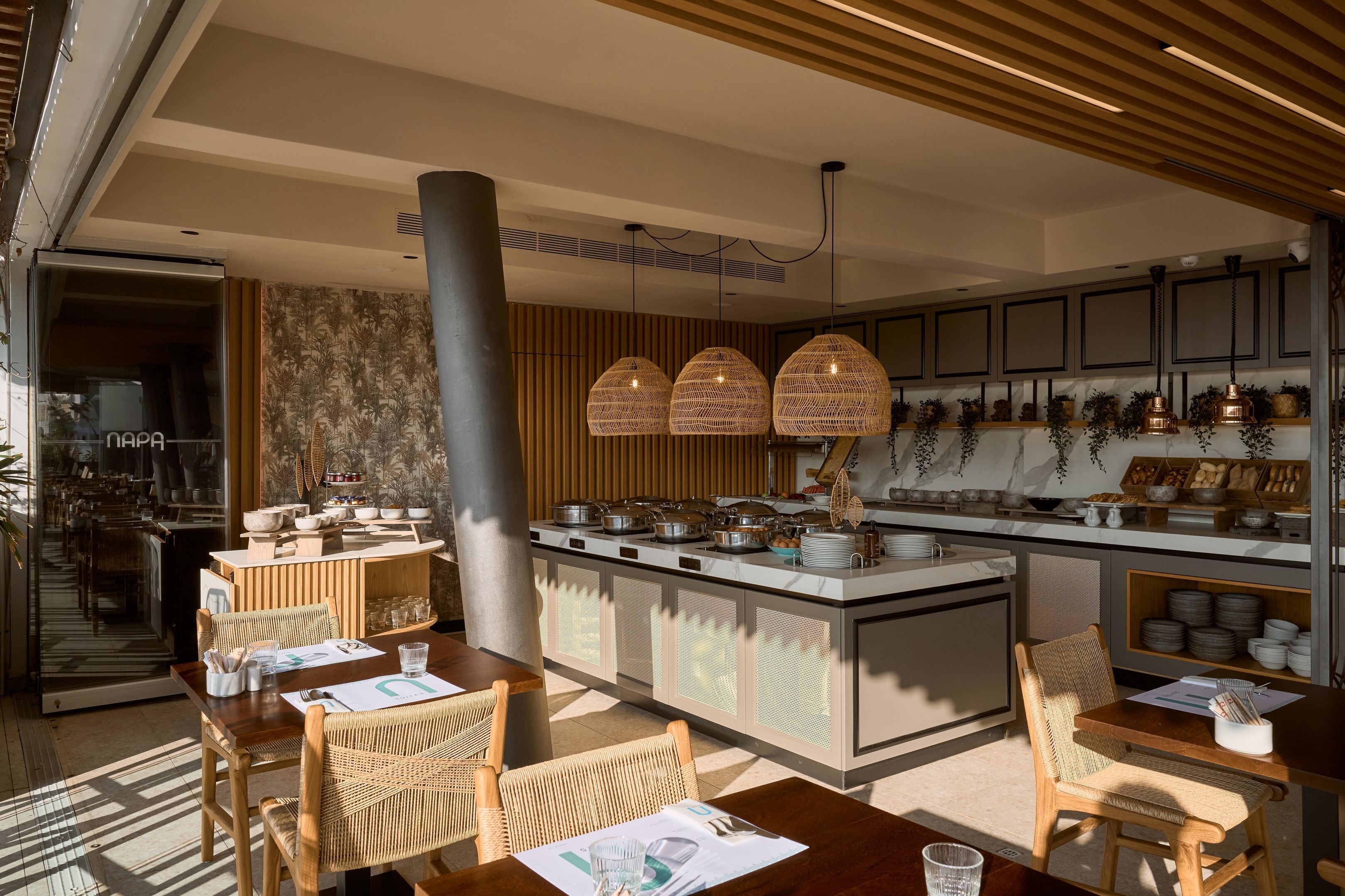 A modern kitchen with a central island, dining area with wicker chairs, and pendant lighting.