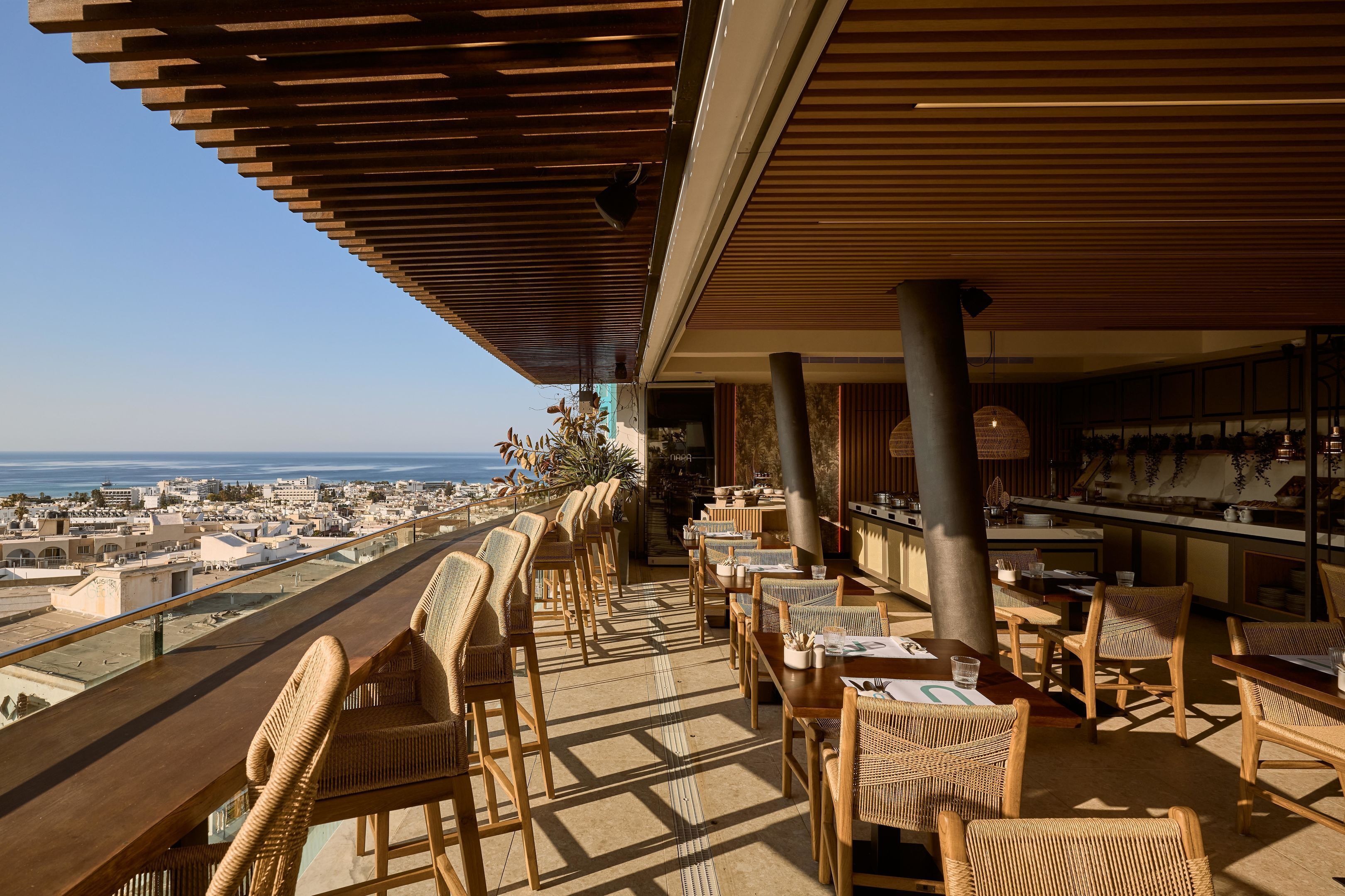 An outdoor dining area with wicker furniture, a view of the city, and a wooden ceiling structure.
