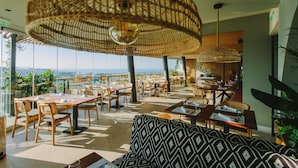 A restaurant with high tables and chairs, large woven ceiling lamps, and a view of the city. - Hotel Napa Suites - Adults Only (Ayia Napa)