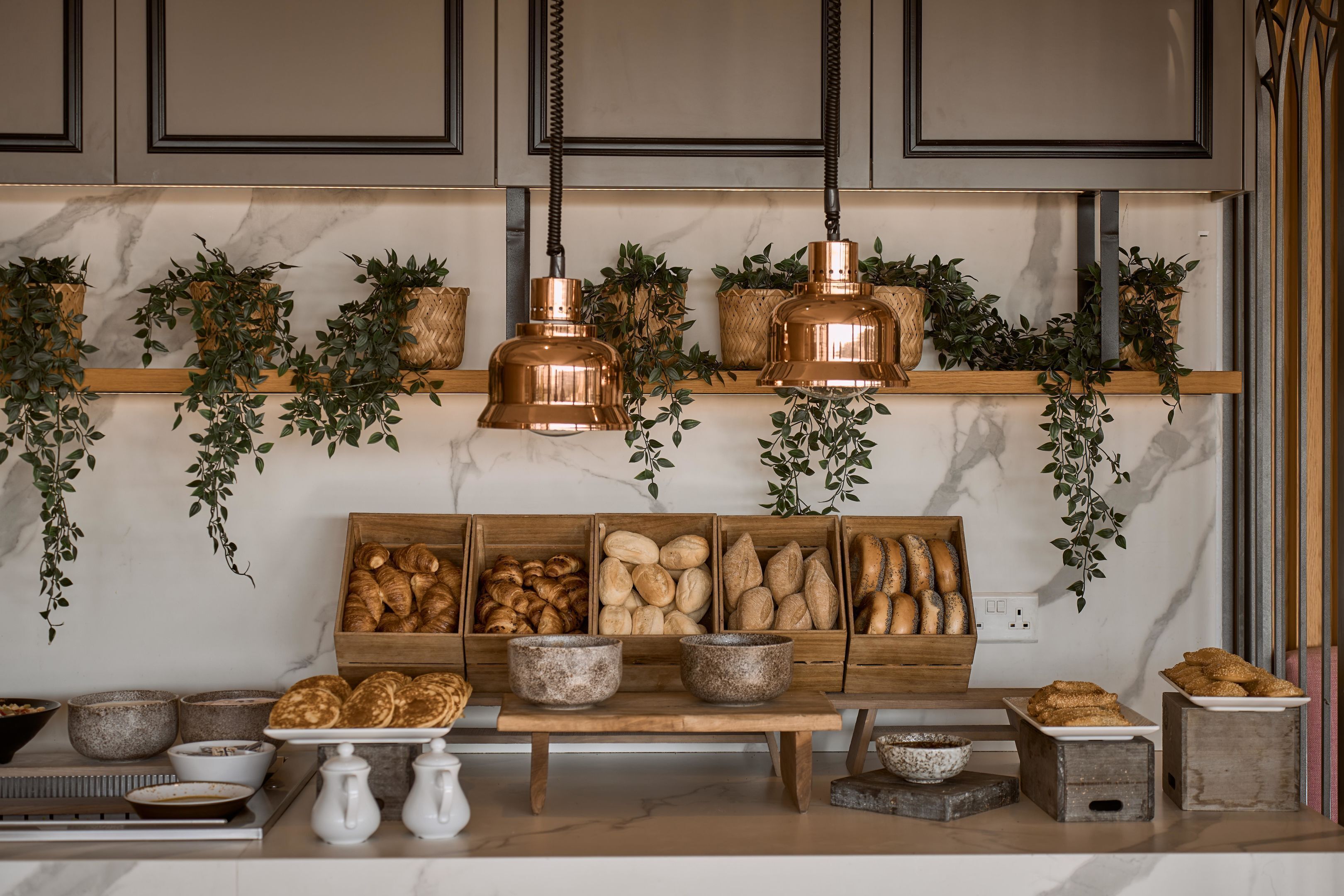 Una cocina con encimeras de mármol, cestas de madera para pan, plantas colgantes y lámparas colgantes de cobre.