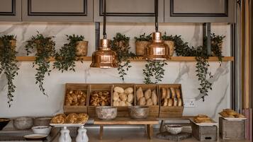 Una cocina con encimeras de mármol, cestas de madera para pan, plantas colgantes y lámparas colgantes de cobre.