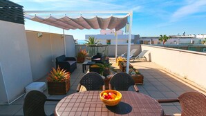 Eine Dachterrasse mit Tisch, Stühlen, Obstschale und Topfpflanzen, mit Blick auf das Meer.