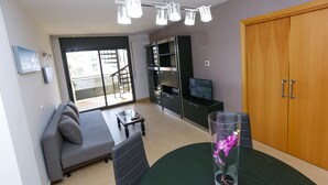 Ein modernes Wohnzimmer mit einer Couch, einem Esstisch, einem Fernseher und einem Kleiderschrank.