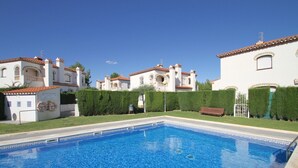 A swimming pool with a tiled deck, surrounded by white buildings with red-tiled roofs and arched windows. - MASIA2 adosado jardín privado, BBQ y piscina comun (Miami Playa)