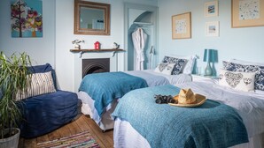 A bedroom with two beds, a mirror, a fireplace, and a potted plant.