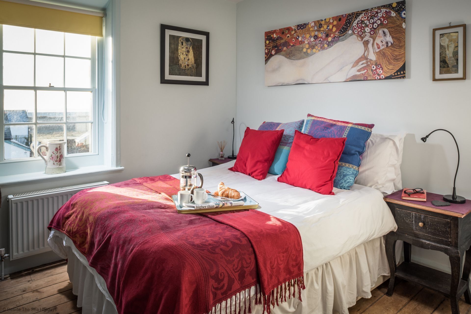 A bedroom with a large bed, a window, a radiator, and a nightstand with a lamp.