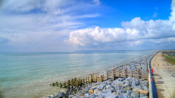 Une promenade en bord de mer, agrémentée d’une clôture en bois et bordée d’une plage rocheuse, qui mène à une plage de sable.