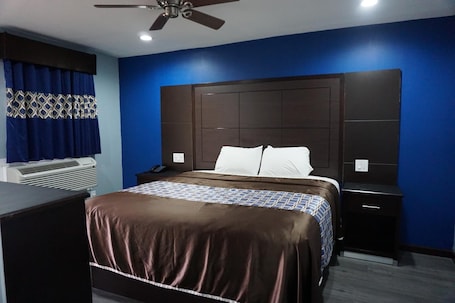 A hotel room with a large bed, a nightstand, a desk, and a ceiling fan.