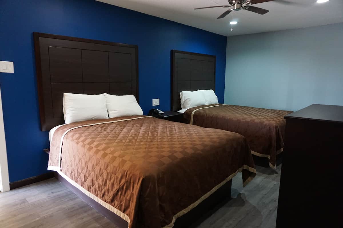 A hotel room with two beds, dark wooden headboards, and a ceiling fan.