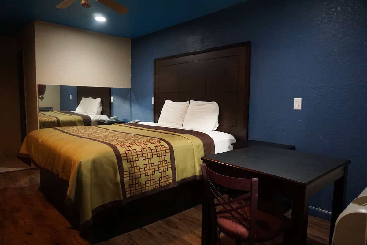 A hotel room with two beds, a wooden floor, a desk with a chair, and a ceiling fan.