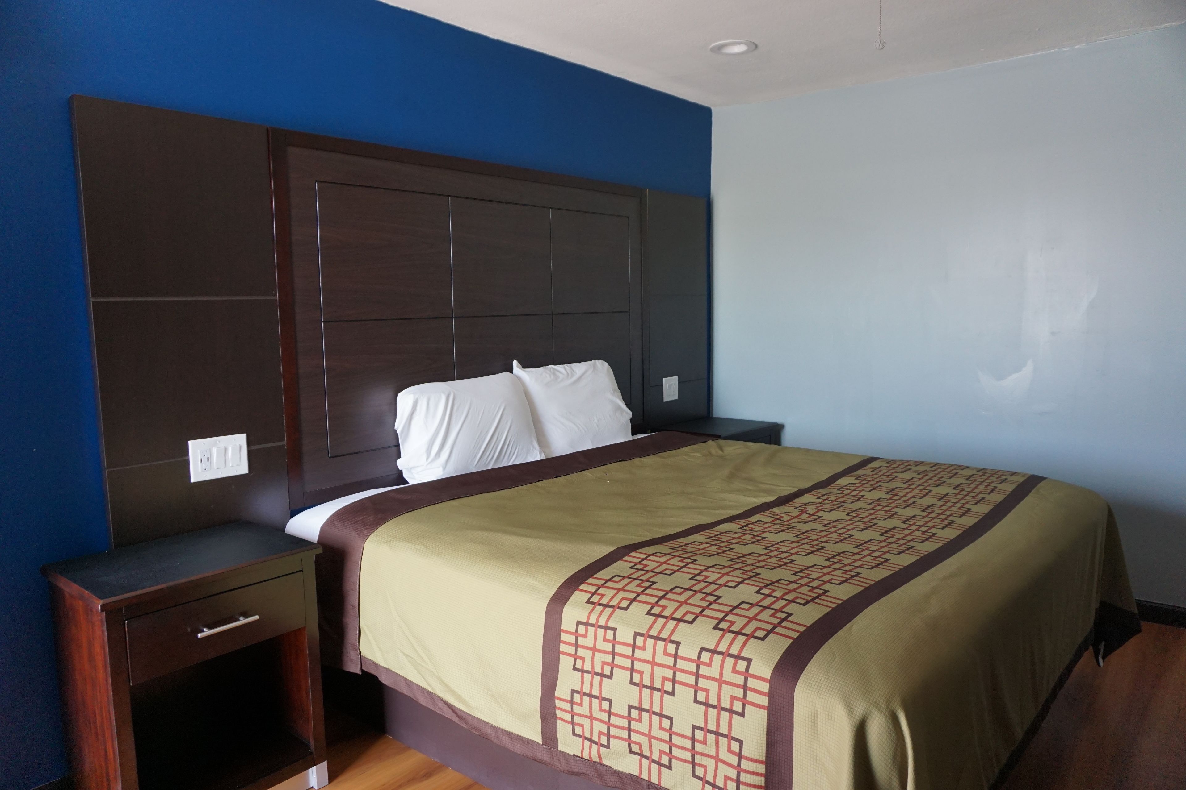 A hotel room with a large bed, a nightstand, a dresser, and a plain wall.