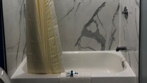 A modern bathroom with a marble shower wall, a bathtub, and a shower curtain. - Star Light Inn (Channelview)