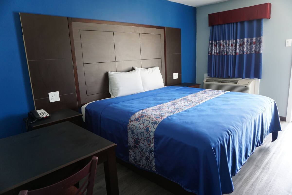 A hotel room with a large bed, a desk, a chair, a telephone, and a window with curtains.