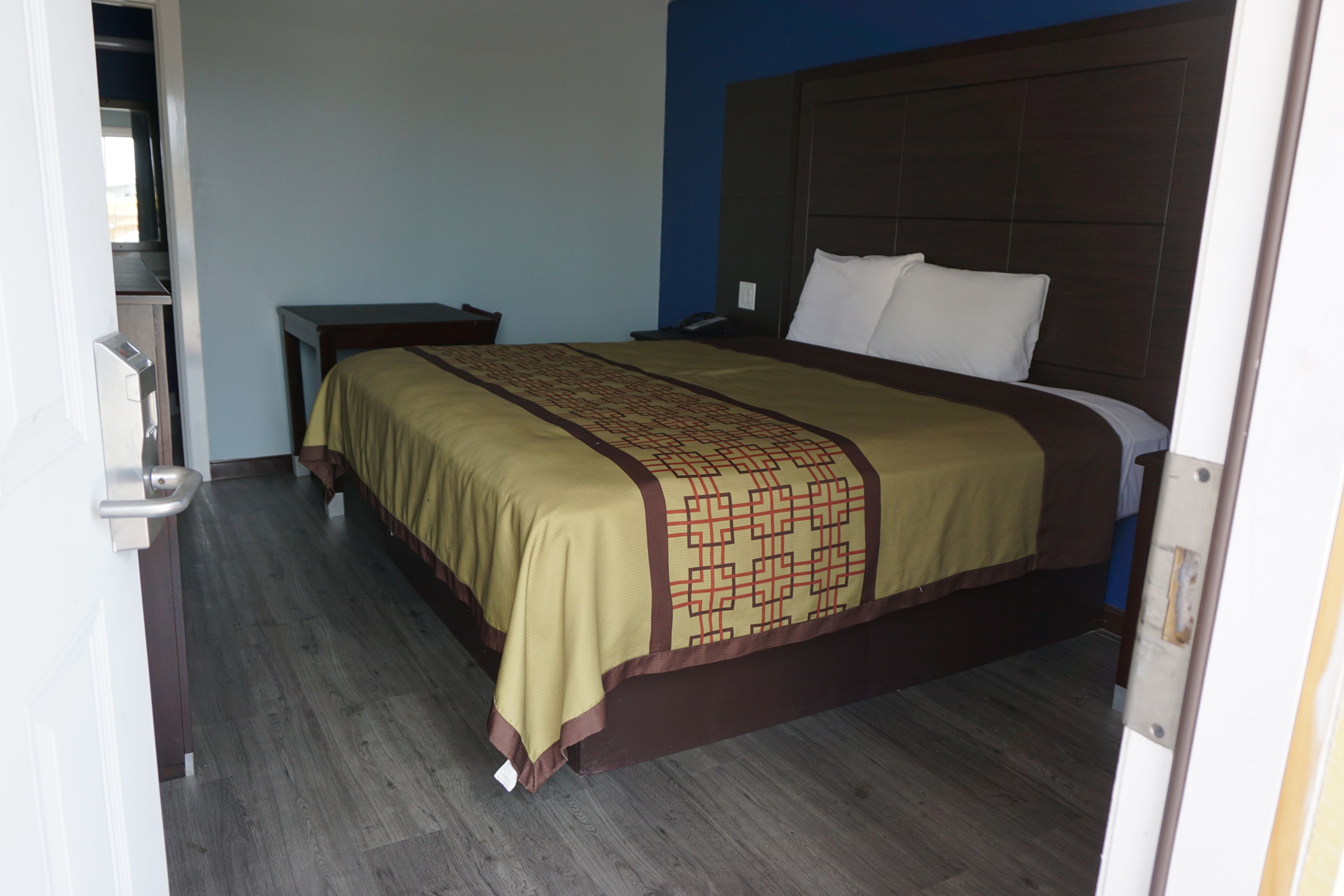 Una habitación de hotel con una cama, una mesita de noche y piso de madera.