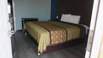 Una habitación de hotel con una cama, una mesita de noche y piso de madera.