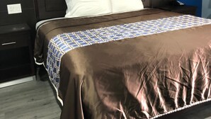 A hotel room with a large bed, a dark headboard, a nightstand with a phone, and a wooden floor. - Star Light Inn (Channelview)