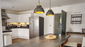 Una cucina moderna con isola centrale, elettrodomestici in acciaio inossidabile, illuminazione a sospensione e una cantina per vini.