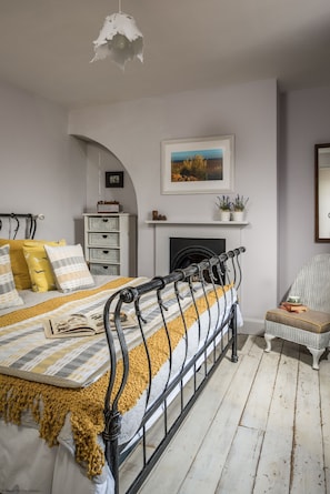 Une chambre à coucher avec un lit, une cheminée, un fauteuil et une étagère avec des plantes.