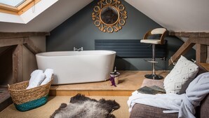 A cozy attic bedroom with a skylight, a large bathtub, a wooden chair, a woven basket, and a fluffy rug. - Coastguards Lookout -  a cottage that sleeps 4 guests  in 2 bedrooms (Jurys Gap)
