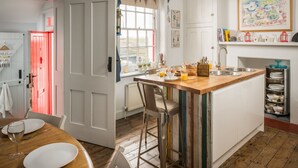 A kitchen with a wooden island, white cabinets, and a red door. There is a window with curtains and a painting on the wall. - Coastguards Lookout -  a cottage that sleeps 4 guests  in 2 bedrooms (Jurys Gap)