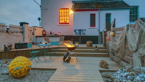 A wooden deck with outdoor seating, a fire pit, and decorative elements like a yellow ball and netting. - Coastguards Lookout -  a cottage that sleeps 4 guests  in 2 bedrooms (Jurys Gap)