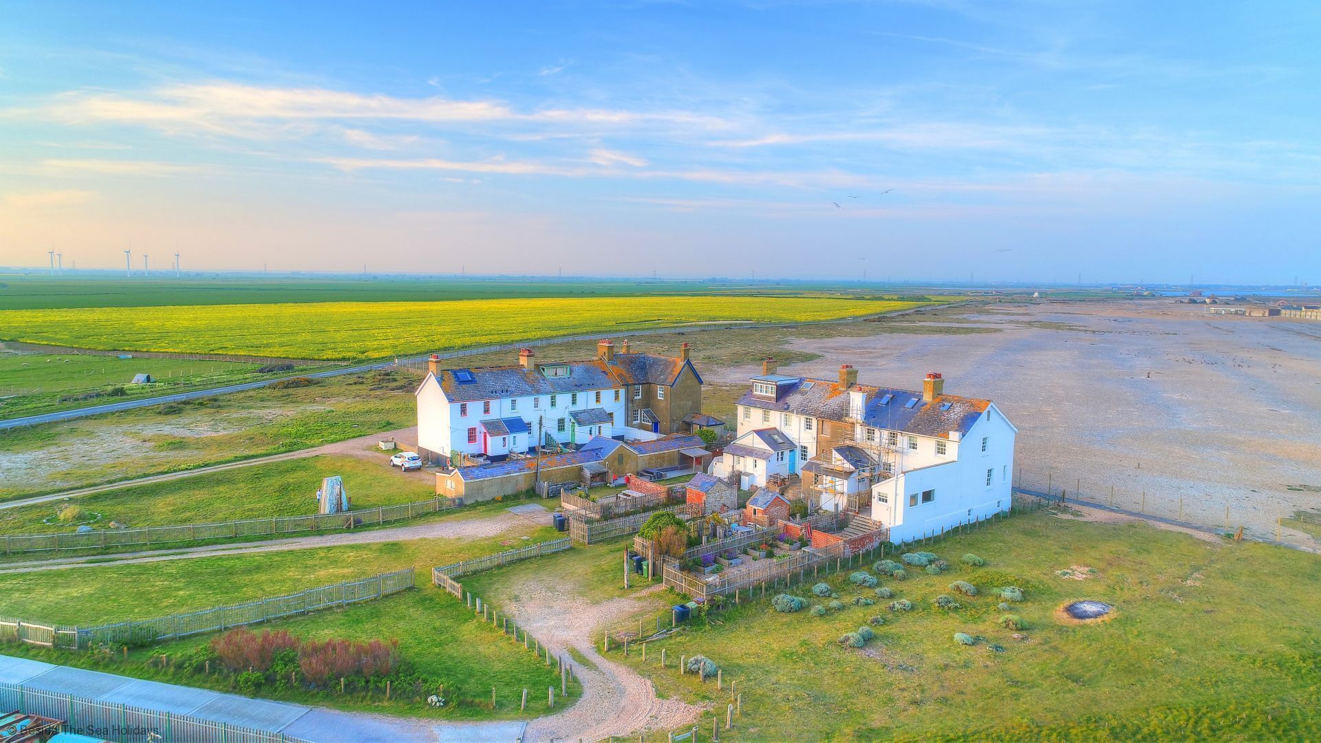 A coastal village with traditional white houses, a sandy beach, and a green field.