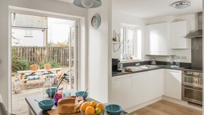 A modern kitchen with white cabinets, a stainless steel oven, and a large window overlooking a garden. - The Beach House -  a cottage that sleeps 6 guests  in 3 bedrooms (Rye)