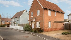 Une rue résidentielle bordée de maisons, dont une maison en briques avec une porte et des fenêtres blanches, et une maison bleue au style similaire.