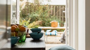 A kitchen with a table set for dining, a hanging light fixture, and a view of the backyard through an open door. - The Beach House -  a cottage that sleeps 6 guests  in 3 bedrooms (Rye)