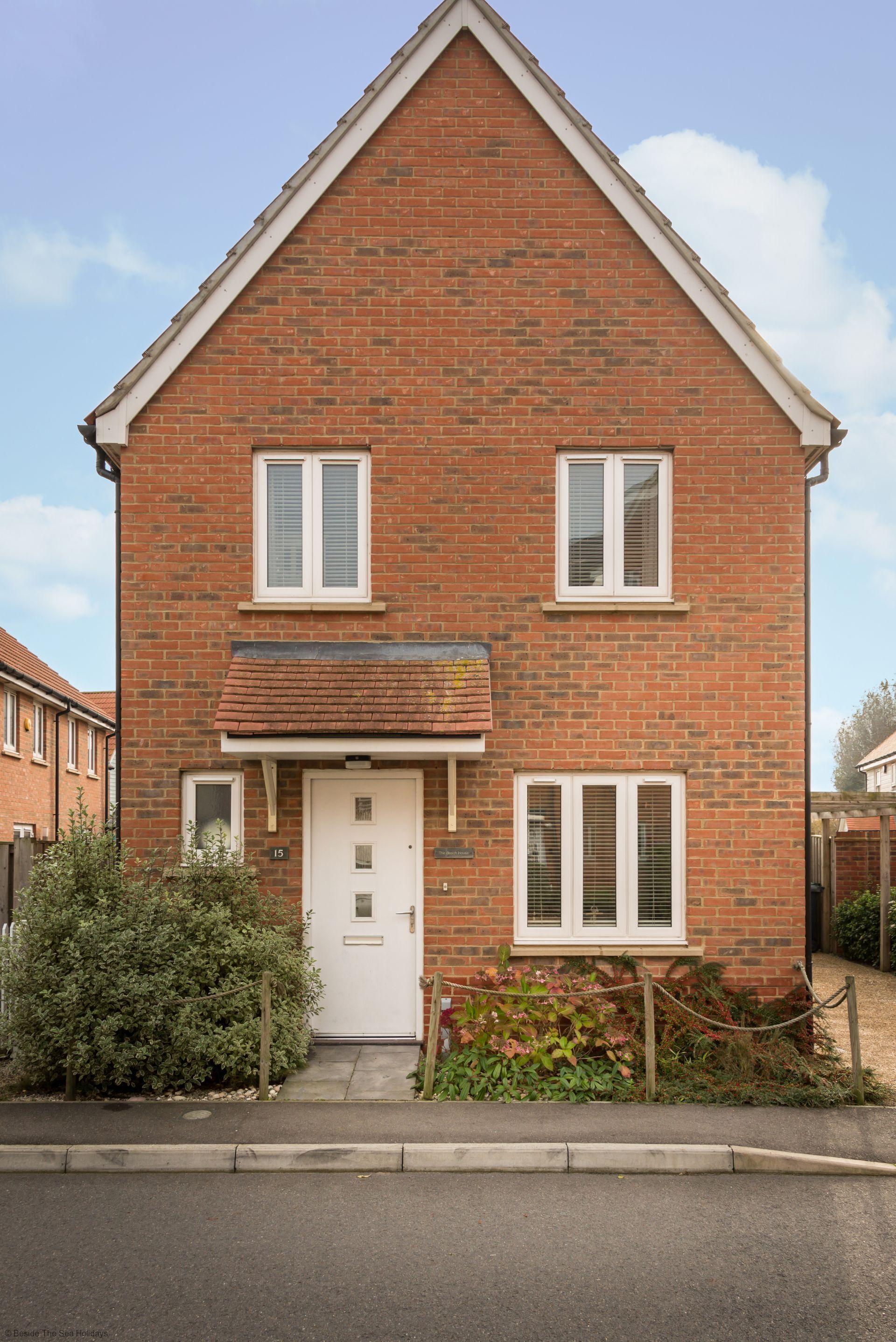 A two-story brick house with a white door, two windows with shutters, and a small front garden.