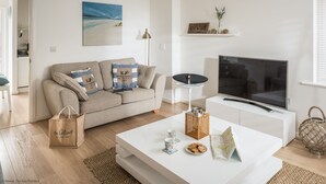 A living room with a sofa, coffee table, TV, and decorative items. - The Beach House -  a cottage that sleeps 6 guests  in 3 bedrooms (Rye)