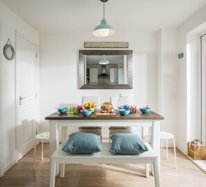 Une cuisine lumineuse avec une table en bois, deux coussins bleus et une suspension.