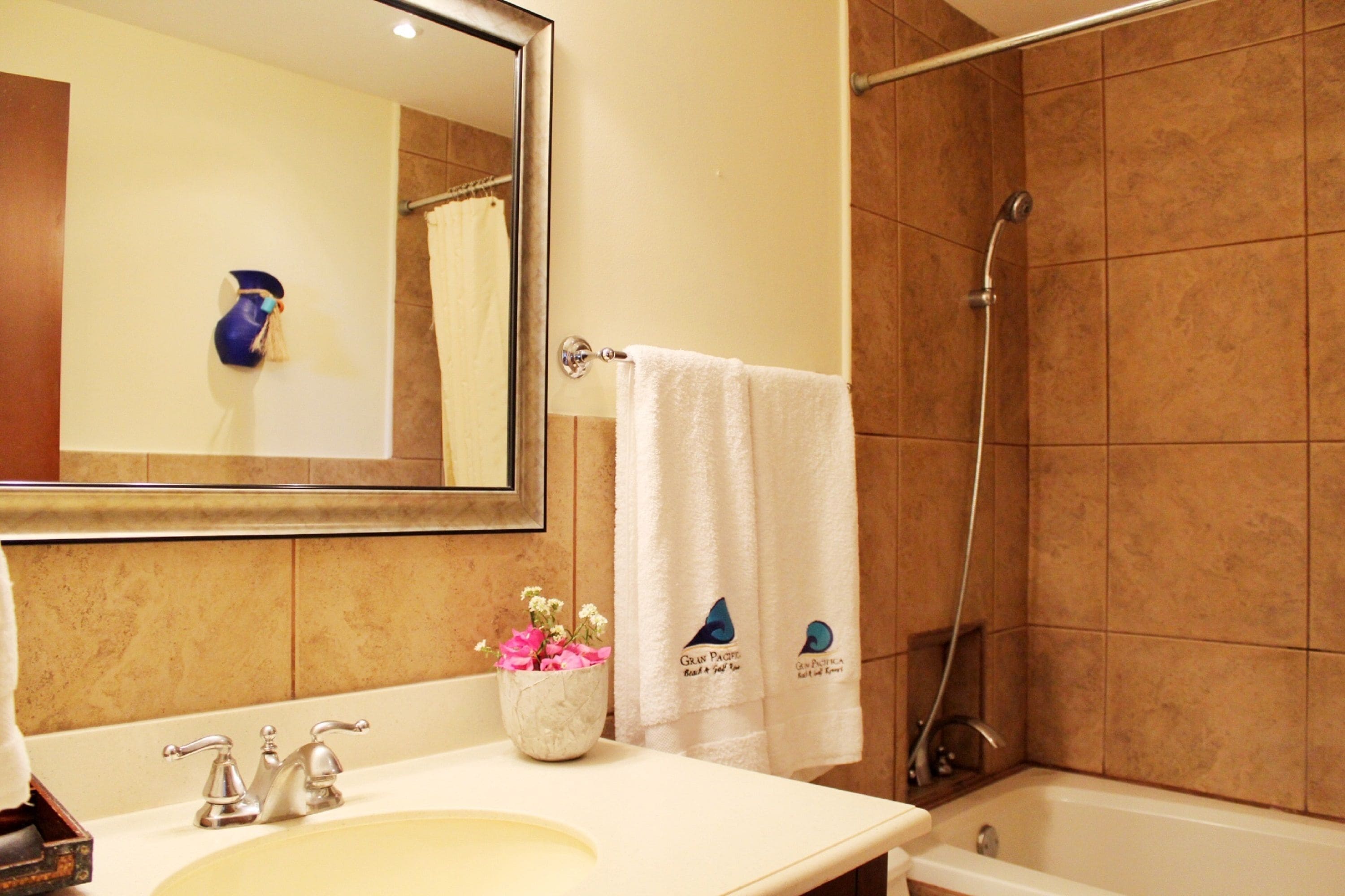 A bathroom with a sink, mirror, towel rack, shower, and a decorative flower vase.