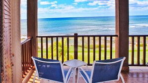 A balcony with two chairs and a small table, overlooking a beach and ocean. - Suite San Juan 135 Gran Pacifica Resort (Villa El Carmen)
